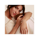 Femme souriante portant un bracelet charm en argent avec pendentifs, mettant en valeur un style élégant.