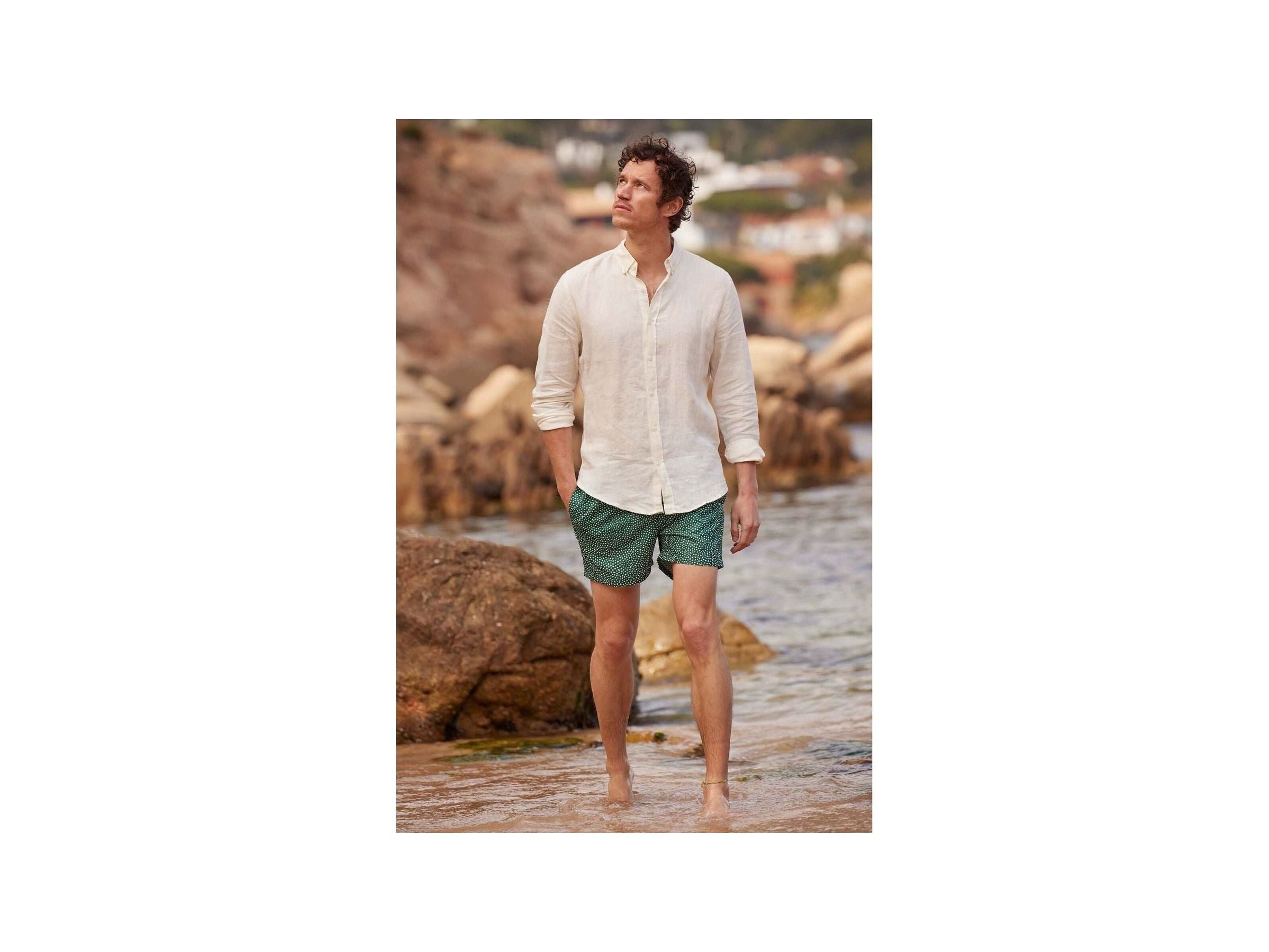 Homme en chemise en lin nature, marchant sur la plage avec un pantalon court, ambiance décontractée.