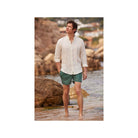 Homme en chemise en lin nature, marchant sur la plage avec un pantalon court, ambiance décontractée.