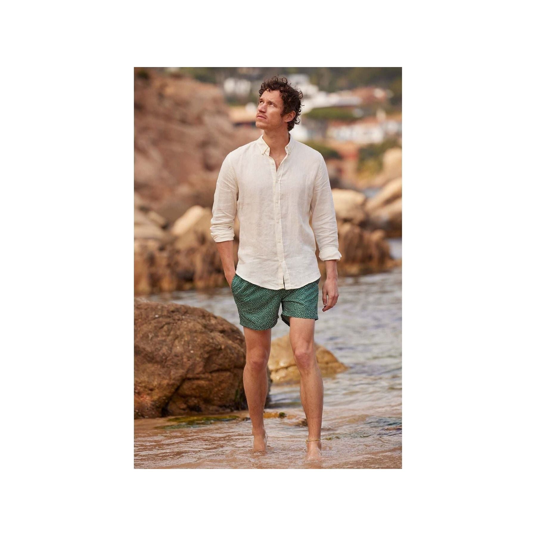 Homme en chemise en lin nature, marchant sur la plage avec un pantalon court, ambiance décontractée.