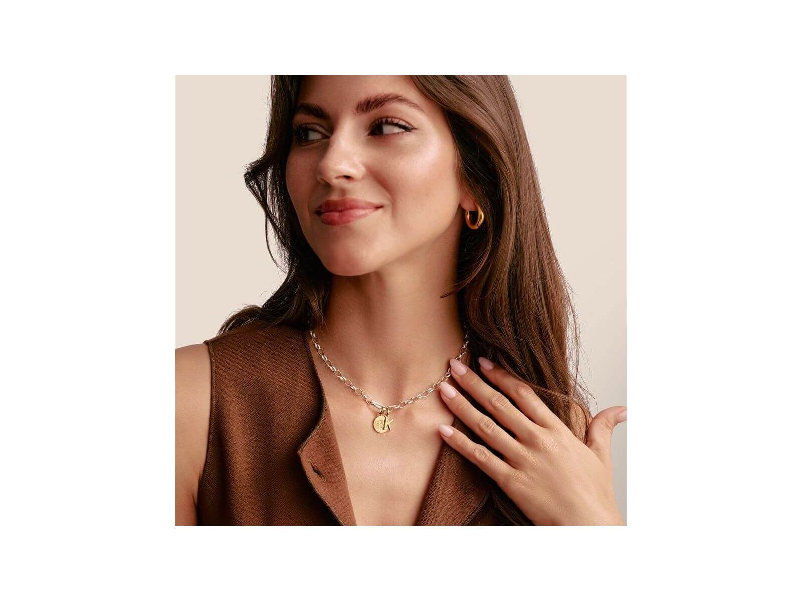 Woman wearing a stylish necklace with a gold charm and hoop earrings, showcasing modern jewelry design.
