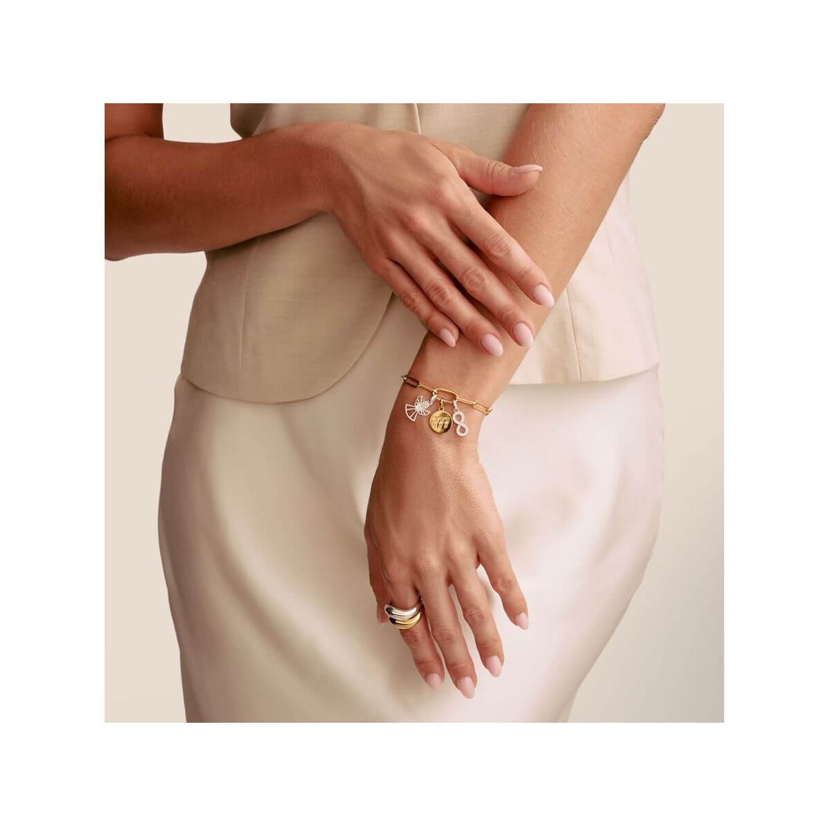 Femme portant un bracelet charm avec symbole infini et pendentifs en argent et or, mettant en valeur l'élégance et le style.