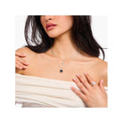 Femme portant une chaîne avec pendentif cœur noir et croix en argent sur un décolleté élégant.