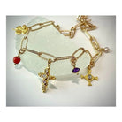 Collier Mystique en plaqué or 24 carats, orné de pendentifs croix et pierres colorées, sur fond de pierre blanche.