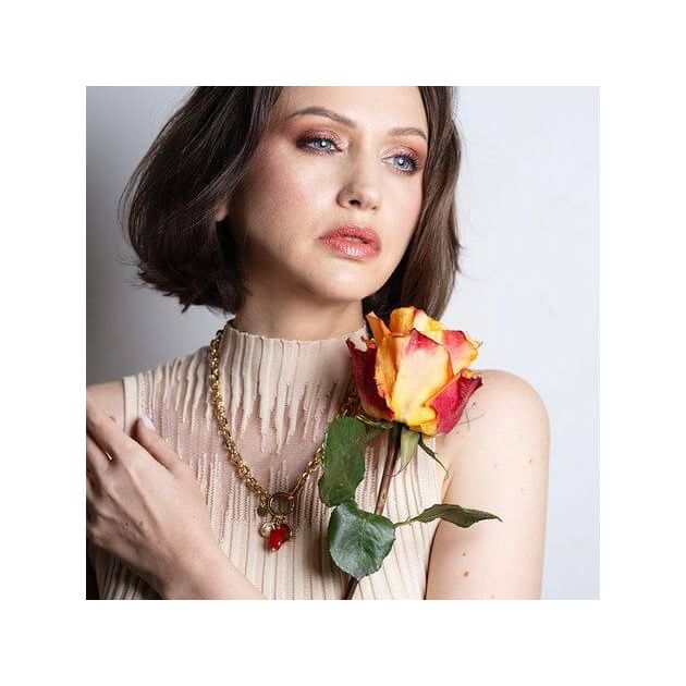 Model showcasing Collier Madone necklace with coral bead, styled with a vibrant rose.