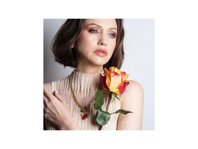 Model showcasing Collier Madone necklace with coral bead, styled with a vibrant rose.