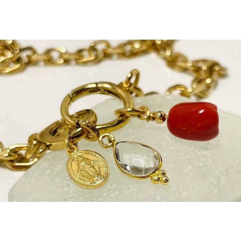 Collier Madone bracelet featuring gold links, red coral bead, and a clear gem on a light stone background.