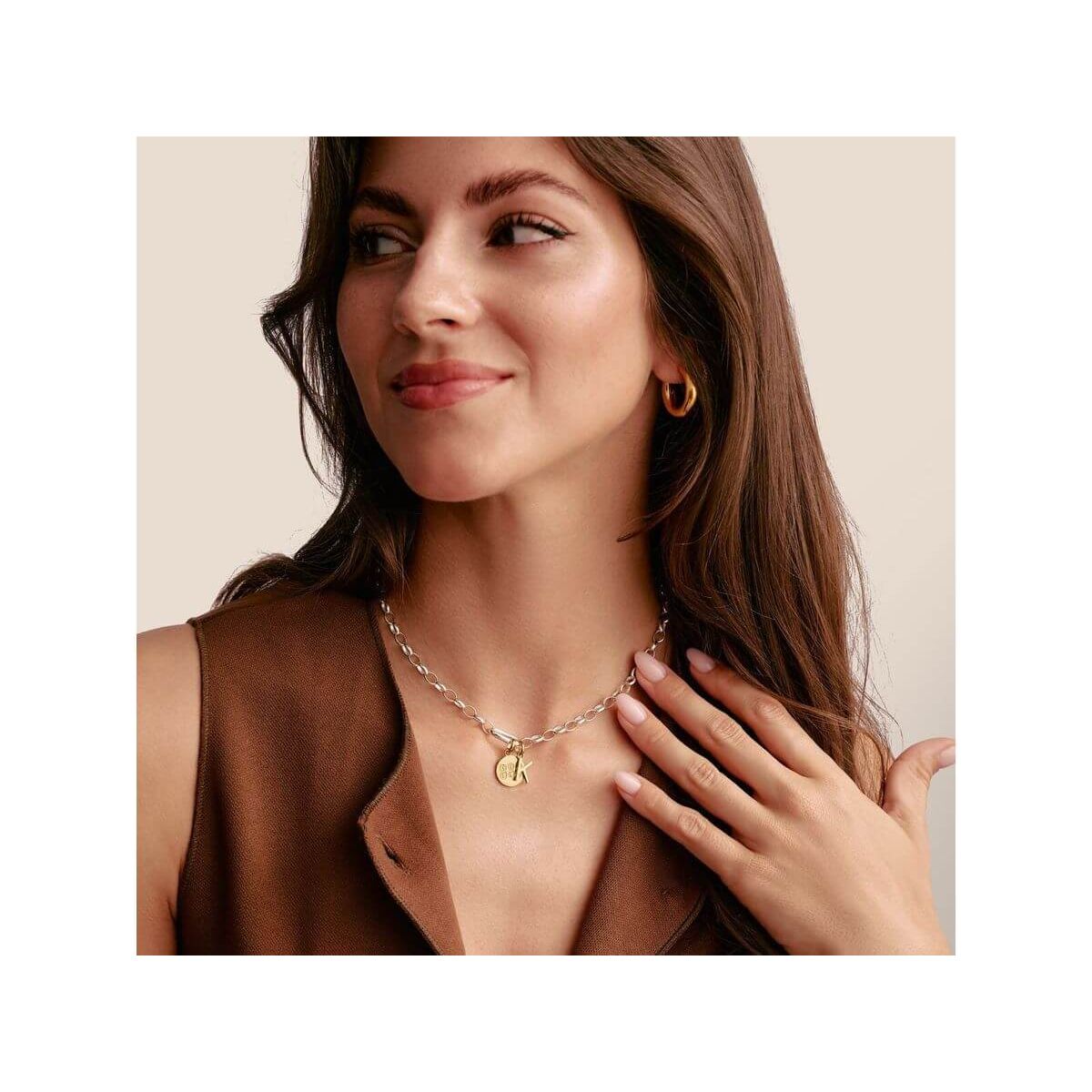 Femme souriante portant un collier chaîne avec un pendentif en or, affichant un style élégant et moderne.