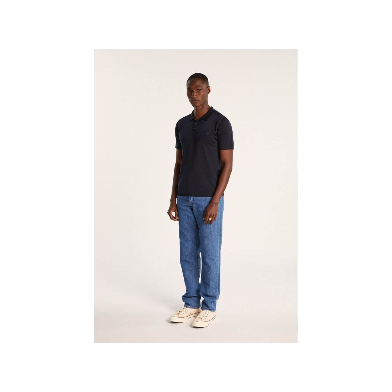 Man wearing a navy short-sleeve polo and blue jeans, showcasing modern casual style.