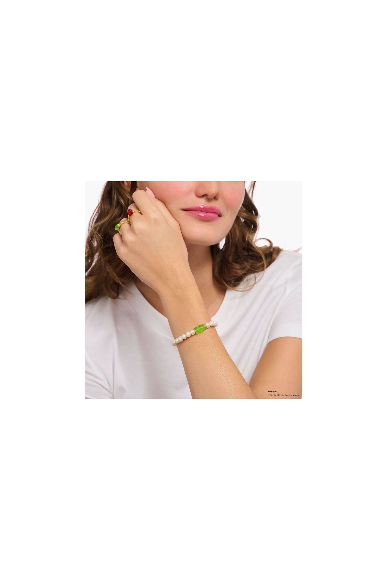 Bracelet de perles d'eau douce avec ours d'or vert sur le poignet d'une femme, style unique et original.