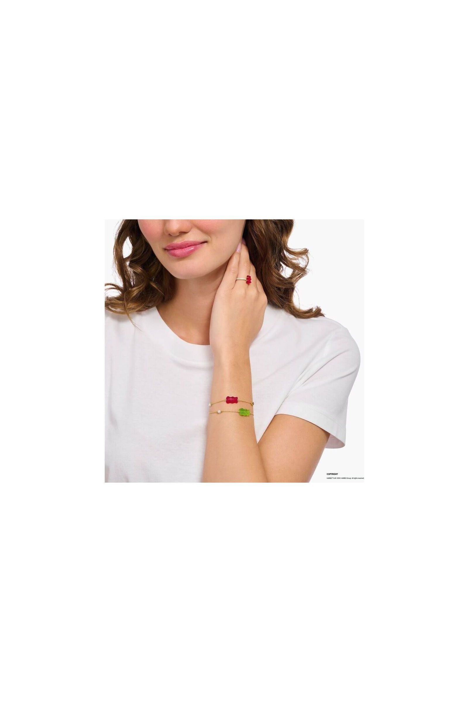 Femme portant un bracelet fantaisie avec ours d'or vert et perles, évoquant l'élégance et la nostalgie.