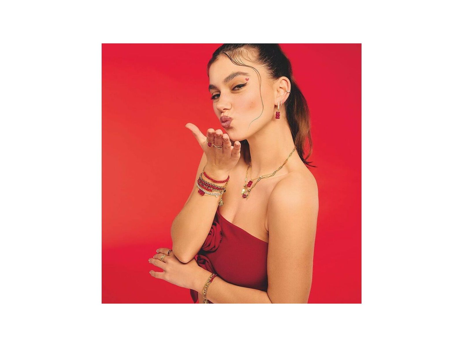 Femme faisant un geste de baiser, portant un bracelet avec Ours d’or rouge et autres bijoux raffinés.