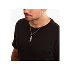 Homme portant un pendentif plume en argent sterling noirci, ajoutant une touche d'élégance à son look décontracté.