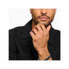 Man wearing a sleek silver band ring and bracelets, showcasing minimalist jewelry style.