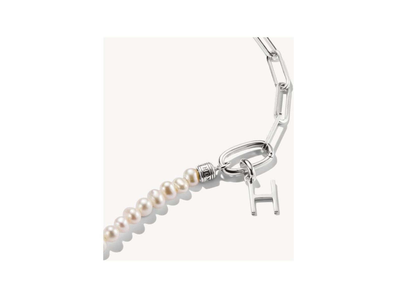 Close-up of a silver charm pendant with a letter 'H' and pearls, perfect for personalized jewelry.
