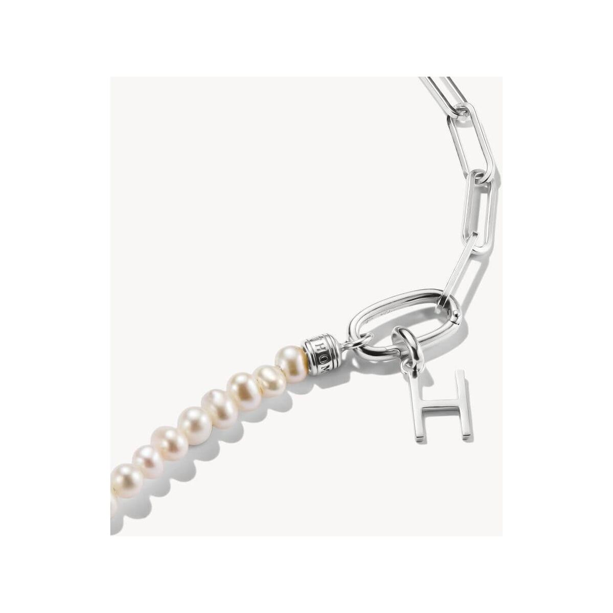 Close-up of a silver charm pendant with a letter 'H' and pearls, perfect for personalized jewelry.