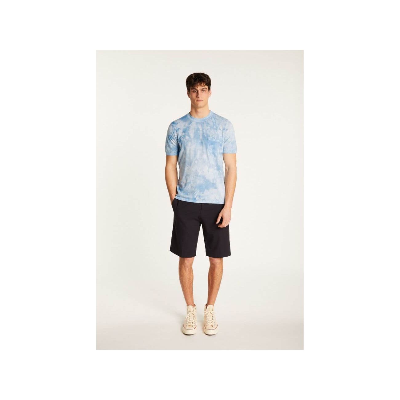 Model wearing a light blue tie-dye T-shirt paired with dark shorts and sneakers.