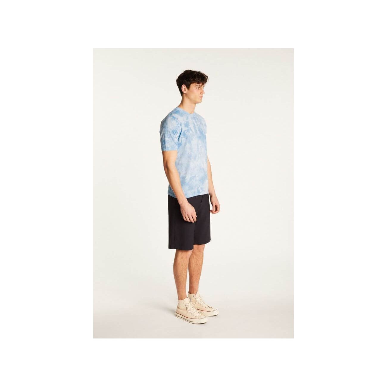 Young man wearing a blue tie-dye T-Shirt and black shorts, showcasing casual summer style.