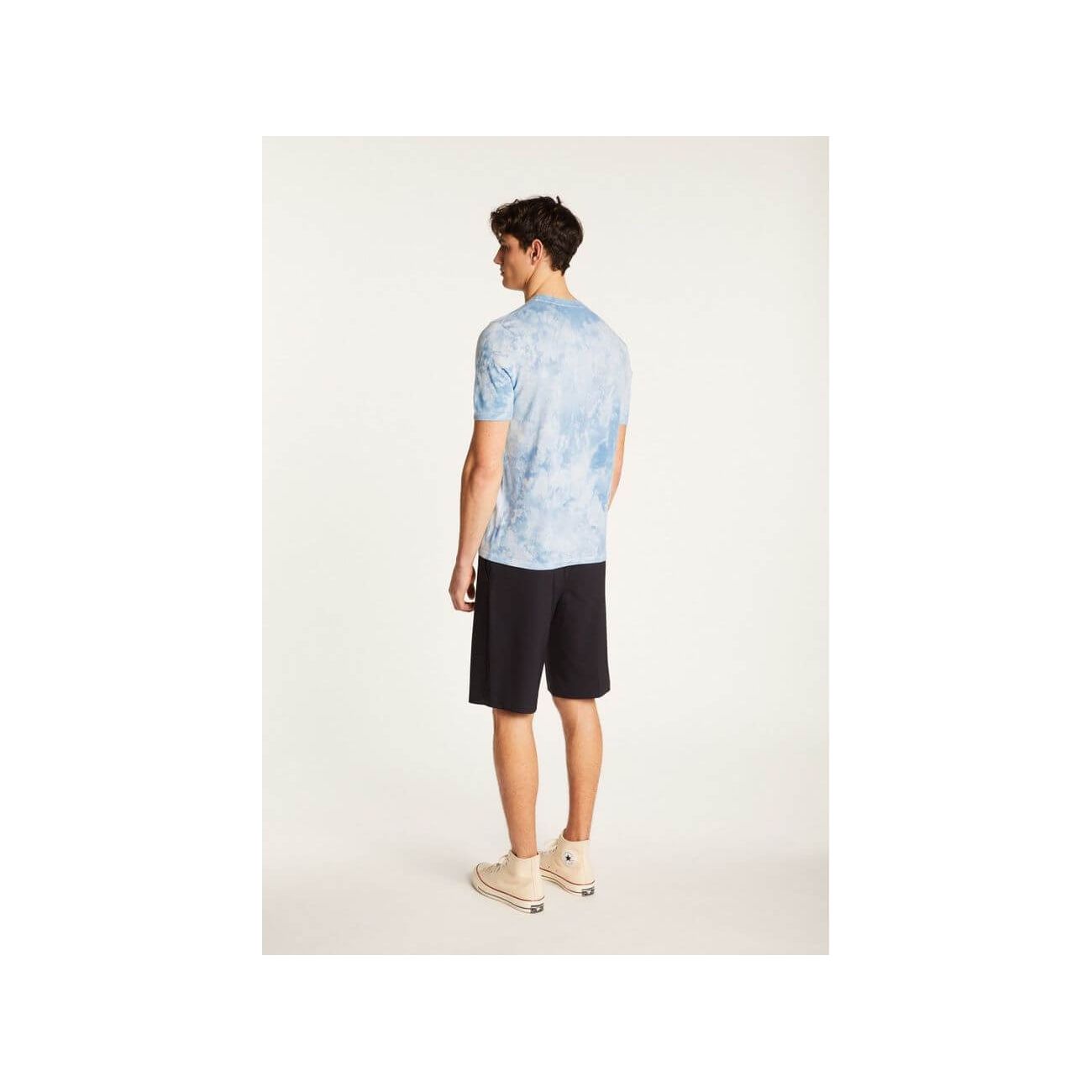 Man wearing a light blue tie-dye T-shirt and black shorts, showcasing a modern casual style from the back.