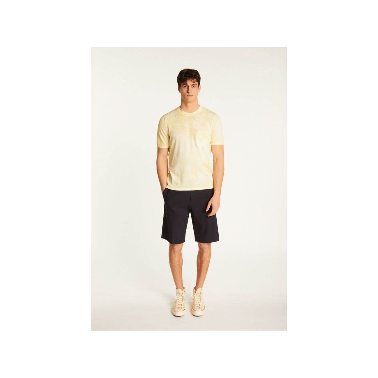 Homme portant un t-shirt jaune clair et un short noir, mettant en avant un look décontracté et élégant.
