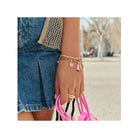 Bracelet charm en argent 925 plaqué or avec charms, porté avec une jupe en denim et un sac rose.