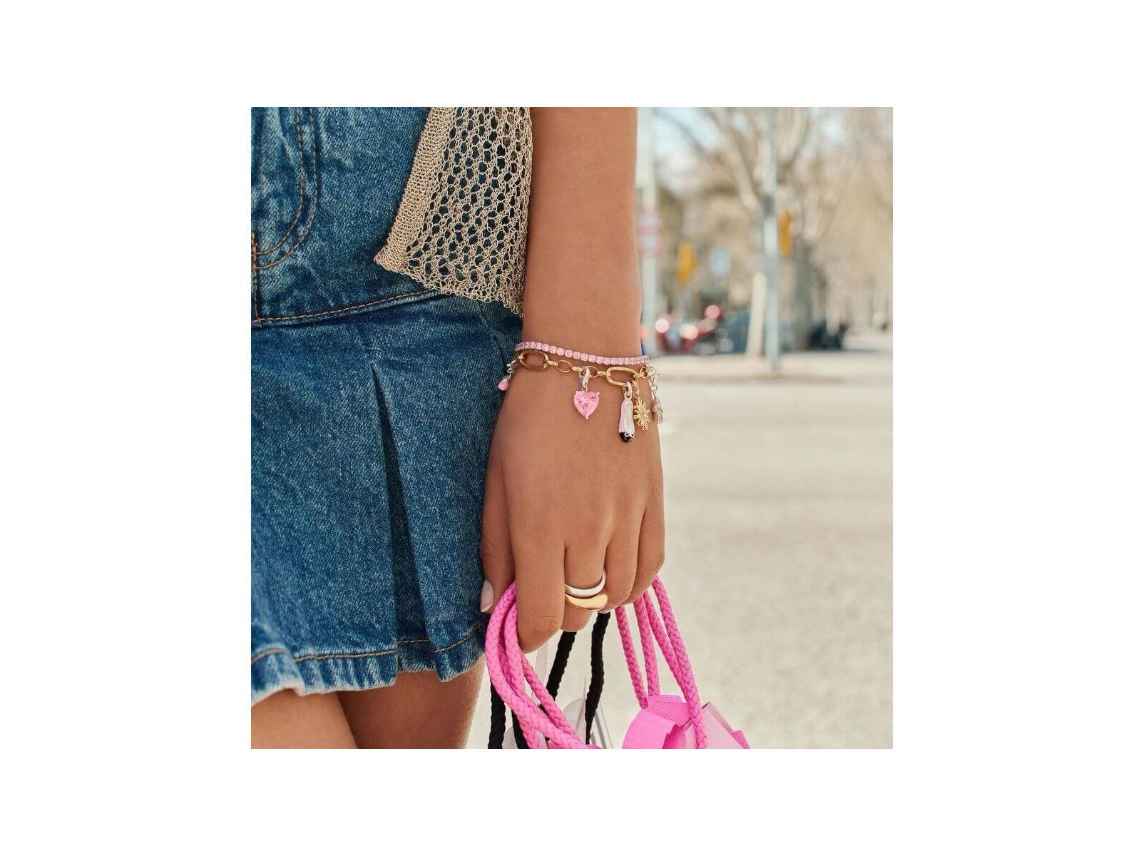 Bracelet charm en argent 925 plaqué or avec charms, porté avec une jupe en denim et un sac rose.