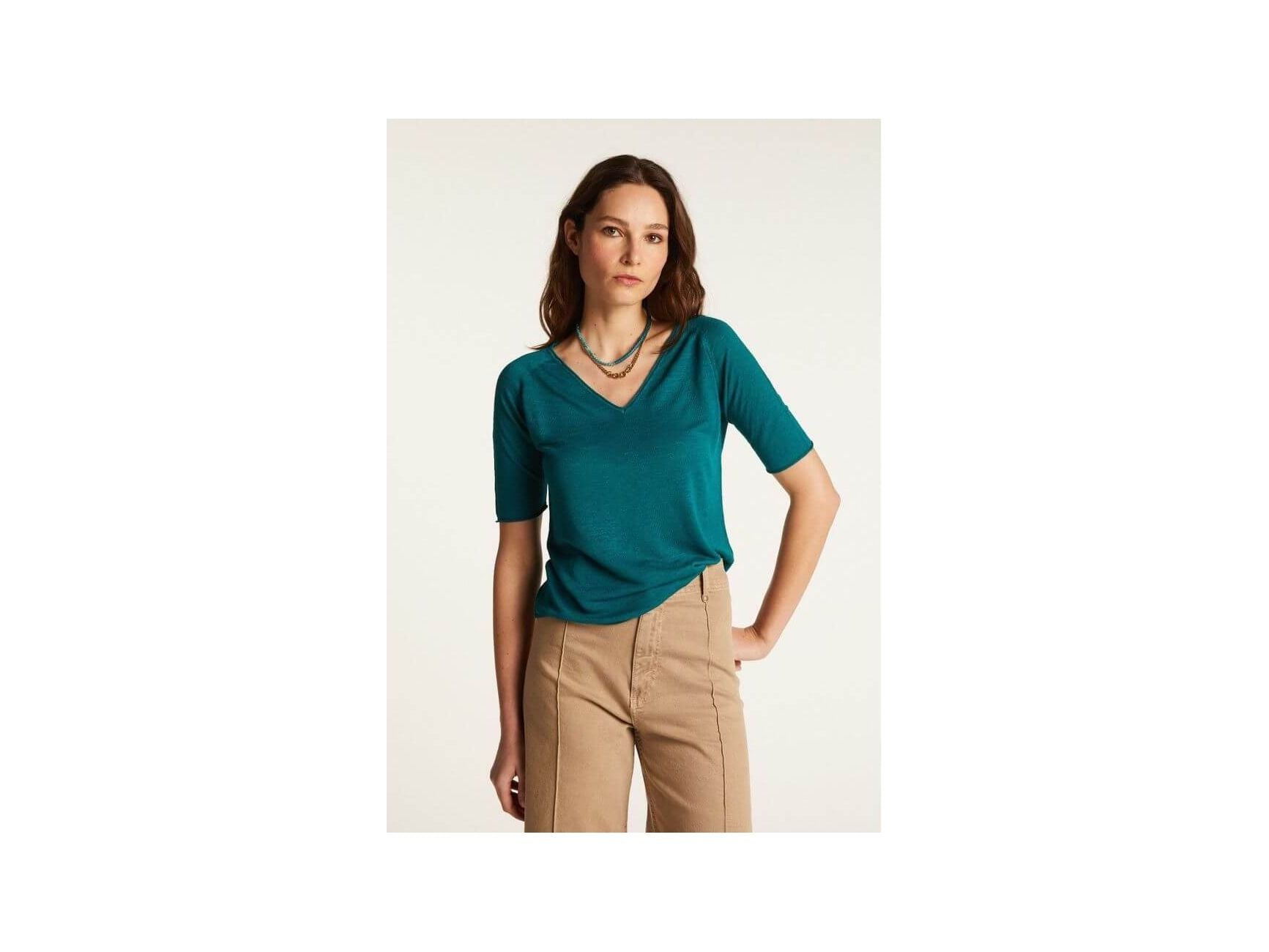 Femme portant un T-shirt teal à col V, en lin léger, associé à un pantalon beige.