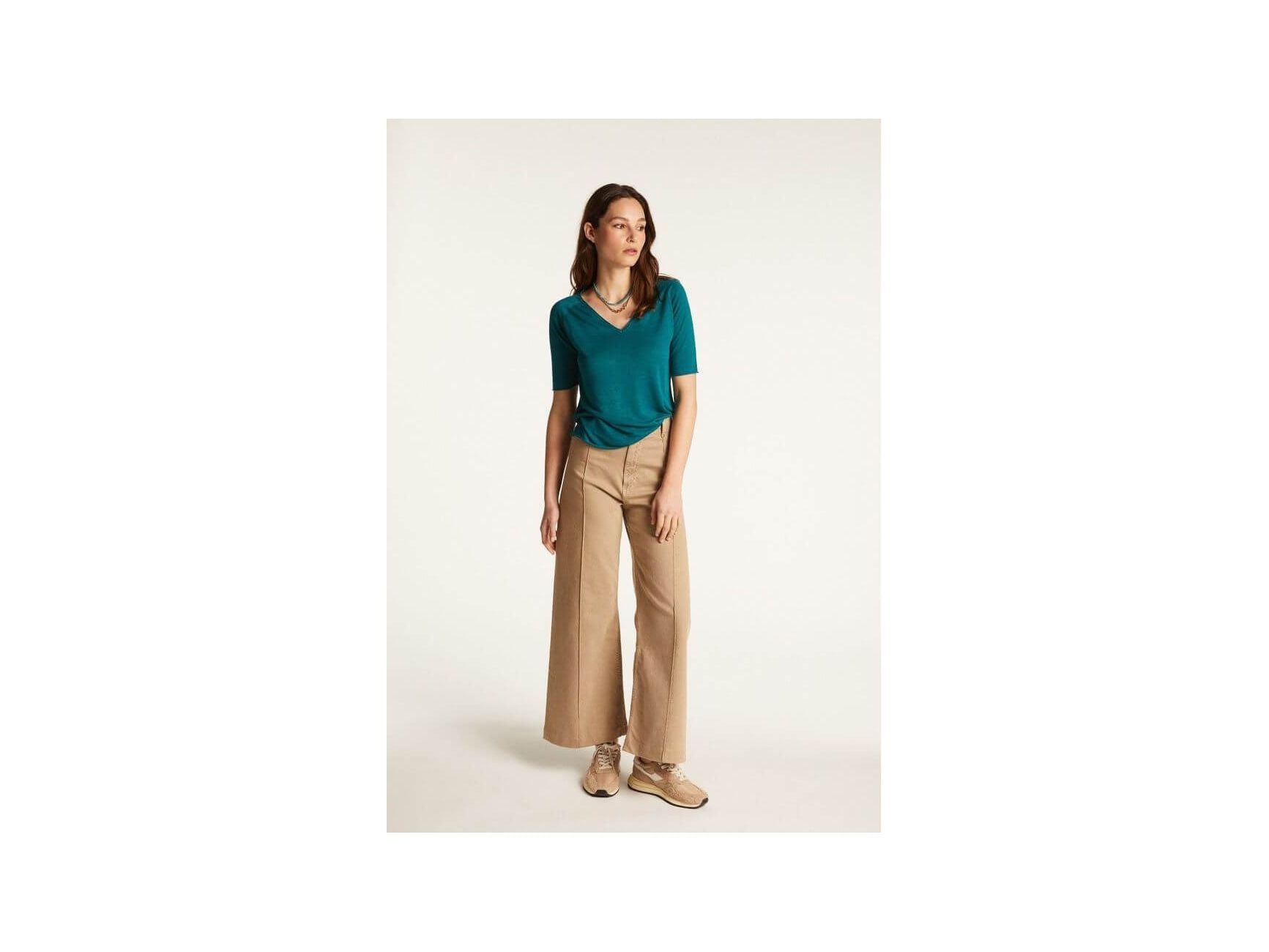 Modèle féminin en t-shirt turquoise et pantalon large beige, parfaite tenue décontractée pour l'été.
