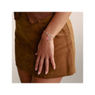 Femme portant un bracelet charm en argent recyclé avec des breloques colorées, sur une jupe marron.