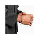 Homme portant un bracelet en argent et des accessoires de mode élégants sur une chemise noire.