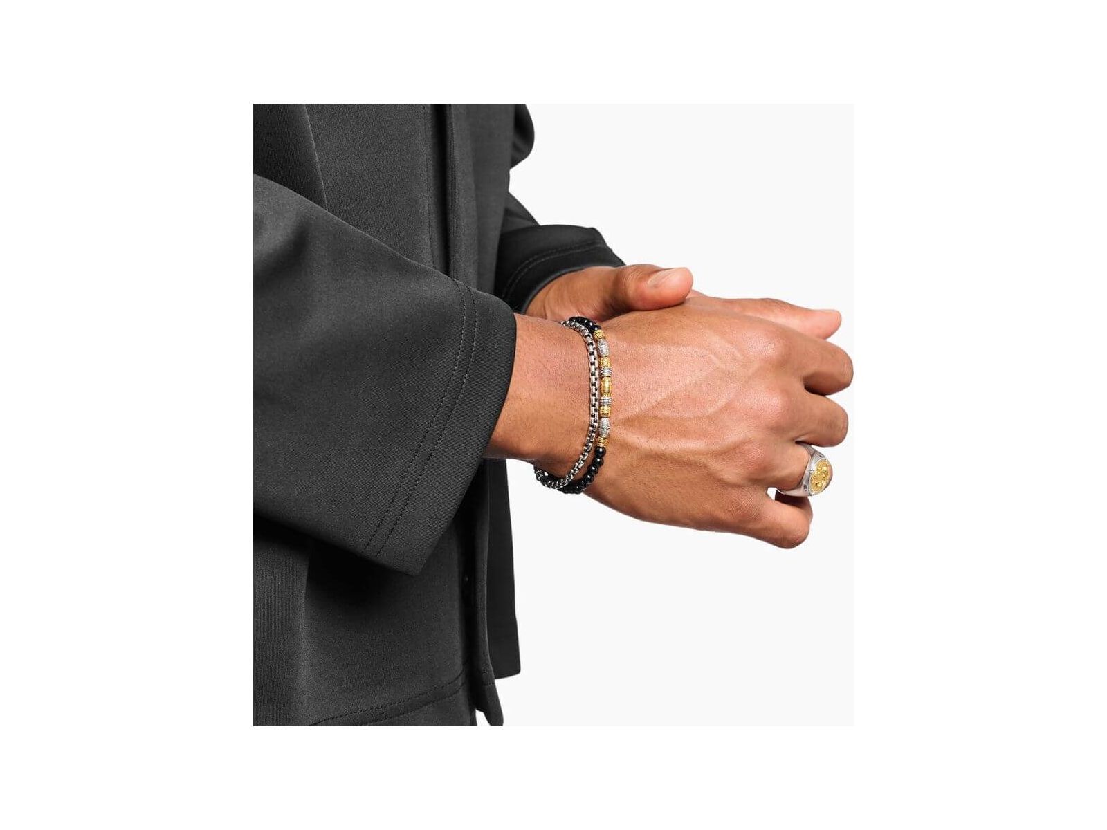 Homme portant un bracelet en argent et des accessoires de mode élégants sur une chemise noire.