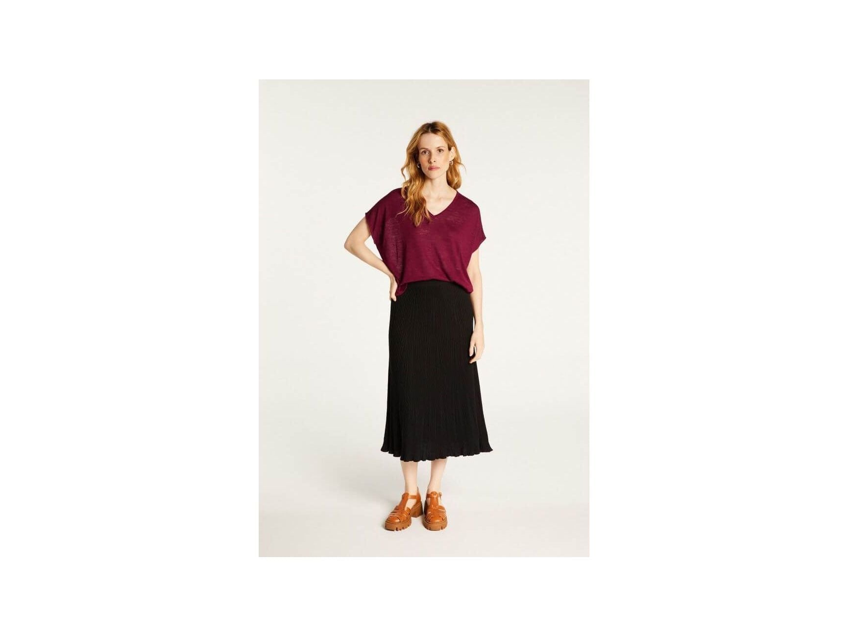 Feminine model wearing Larra V-neck T-shirt in burgundy with black pleated skirt, showcasing elegance and comfort.
