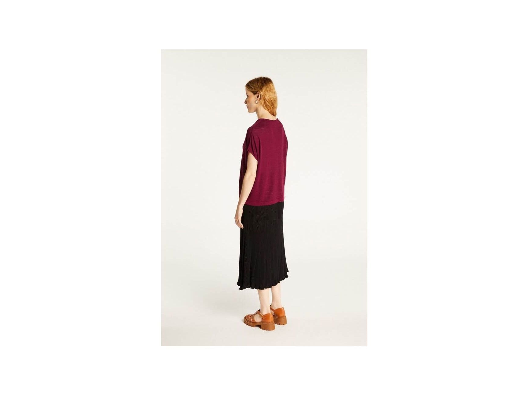 Model showcasing Larra T-shirt in flammé linen, paired with a black pleated skirt, highlighting comfort and style.