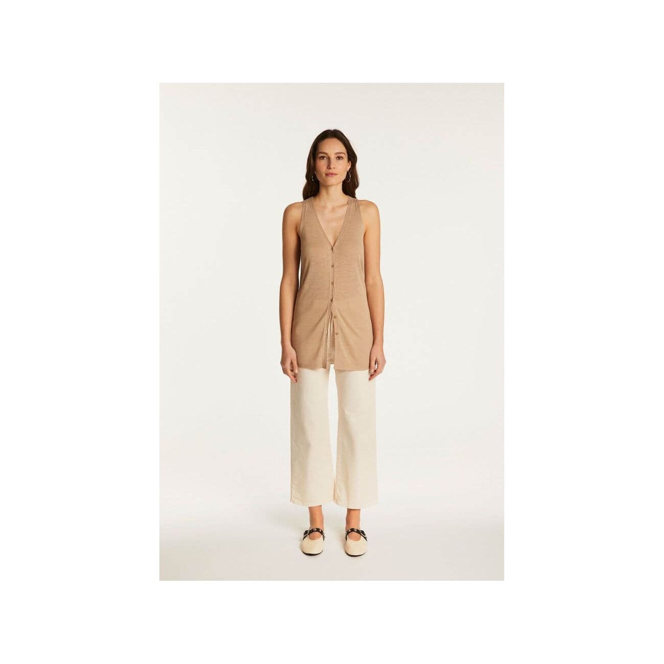 Woman wearing a lightweight linen short-sleeve vest top styled with white trousers for a chic summer look.