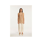 Woman wearing a lightweight linen short-sleeve vest top styled with white trousers for a chic summer look.