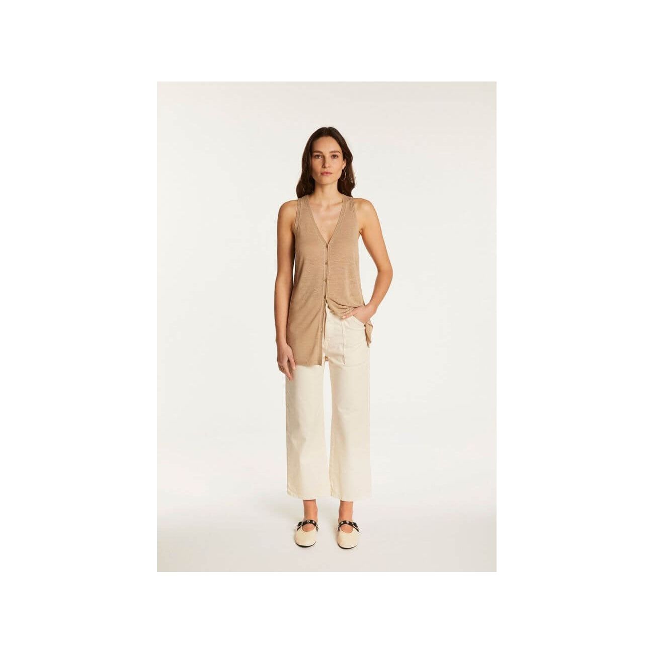 Femme portant un gilet léger à manches courtes en lin flammé, associé à un pantalon blanc, look estival chic.