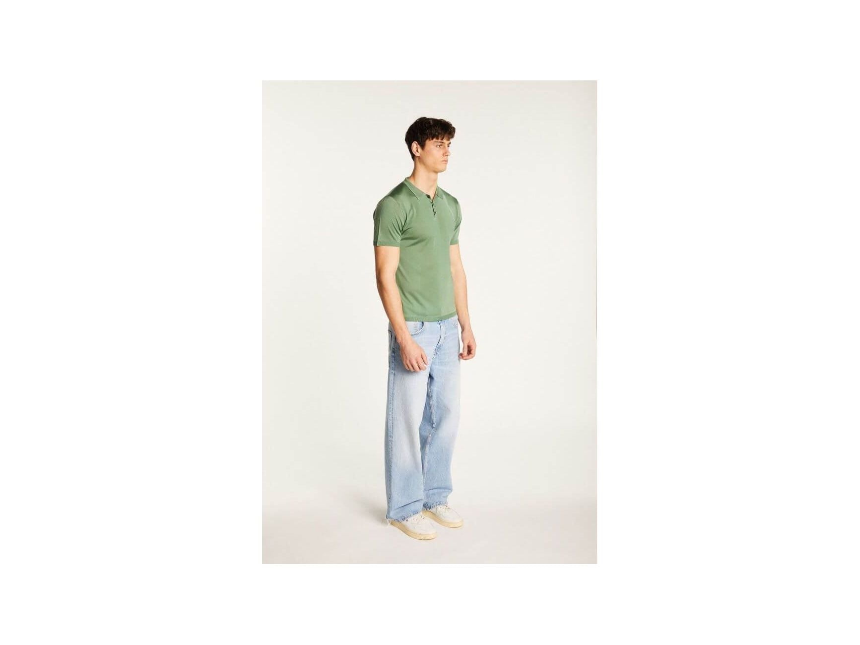 Homme portant un polo vert en fil lumière avec jeans clairs pour un look élégant et décontracté.