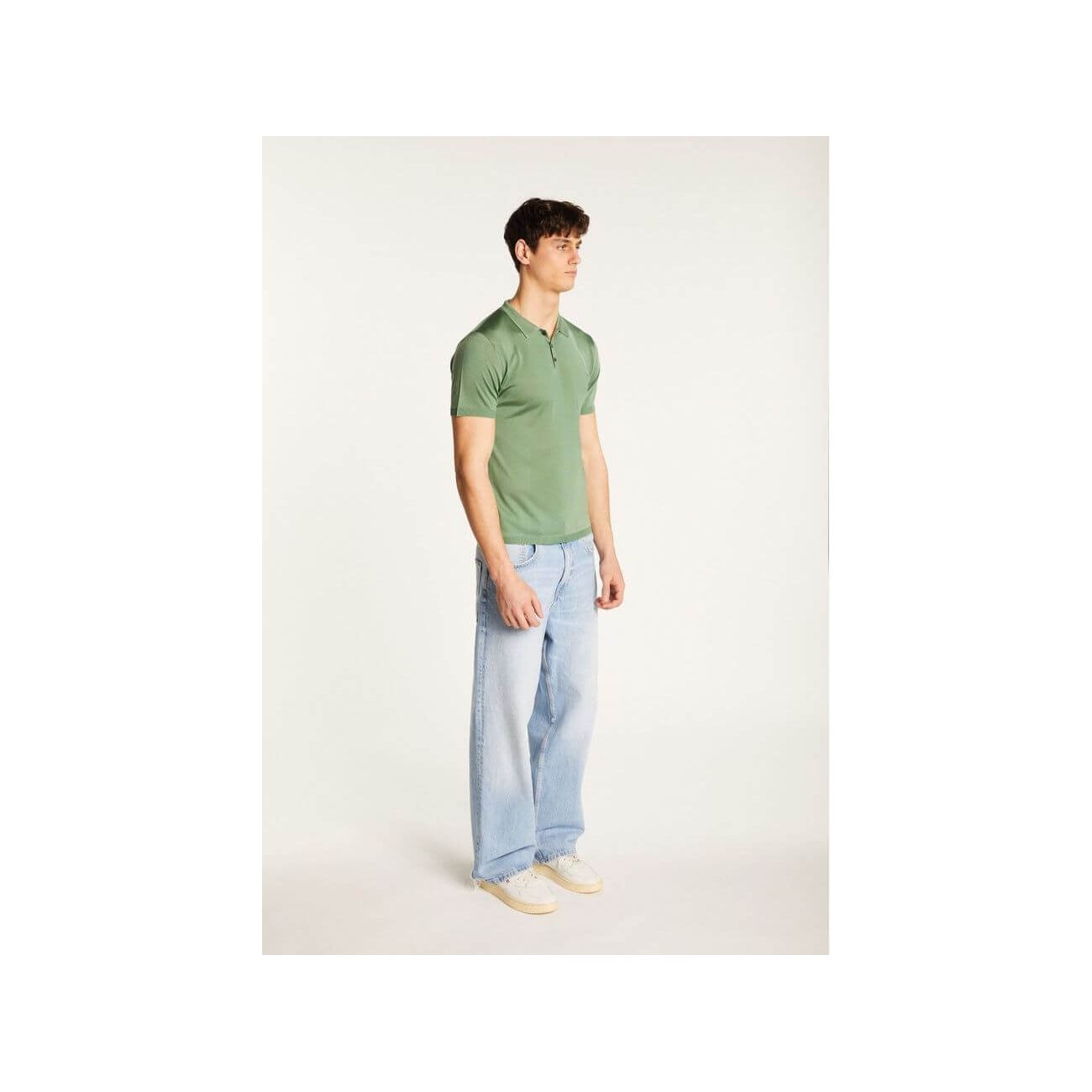 Homme portant un polo vert en fil lumière avec jeans clairs pour un look élégant et décontracté.