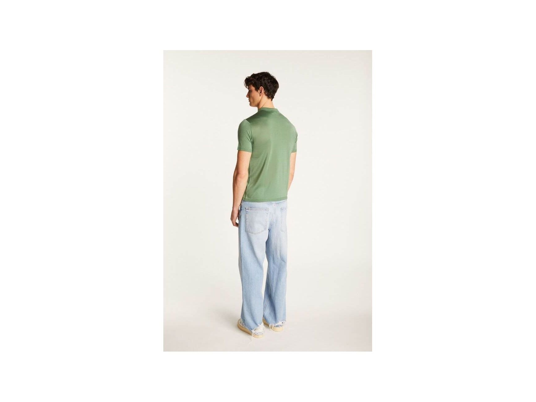Homme portant un polo vert Fil lumière Babar, vu de dos, associé à un pantalon décontracté en denim.