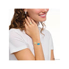 Femme portant un bracelet en argent avec ours d'or bleu et perle, affichant un sourire et des bijoux délicats.