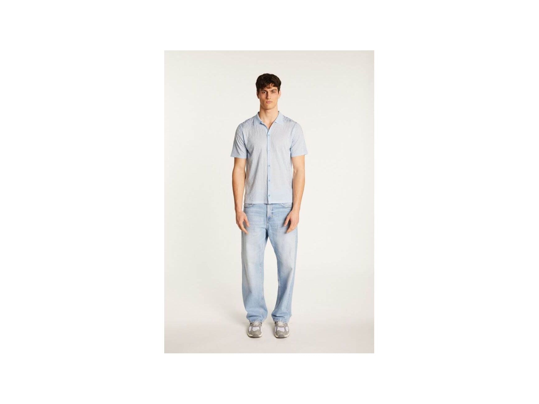 Model wearing the Matthew short-sleeve shirt in blue, paired with light jeans for a casual summer look.