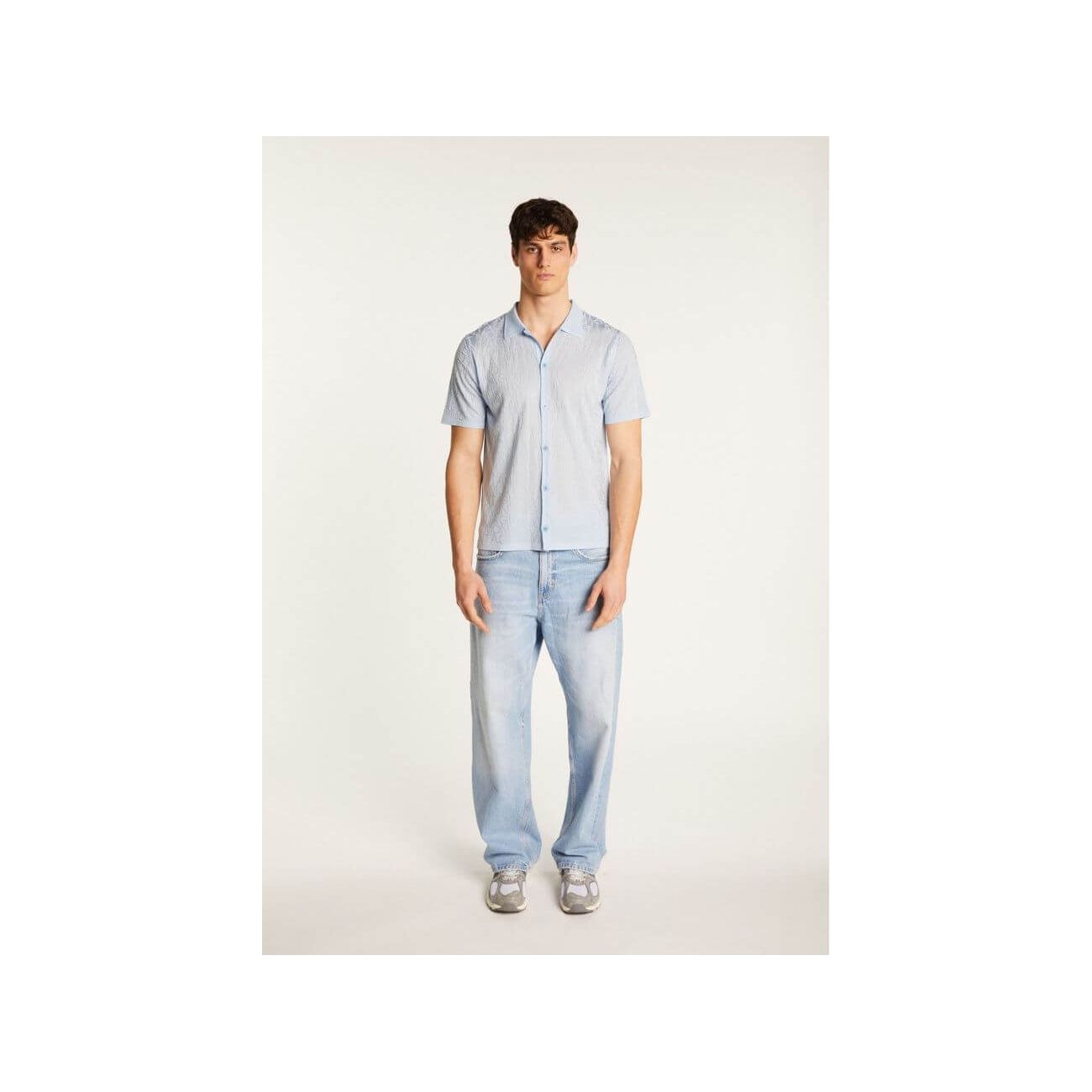 Model wearing the Matthew short-sleeve shirt in blue, paired with light jeans for a casual summer look.