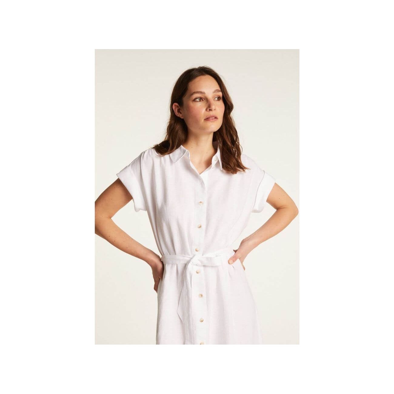 Femme portant une robe blanche Emy en lin léger, dotée de boutons et d'une ceinture pour un look élégant.
