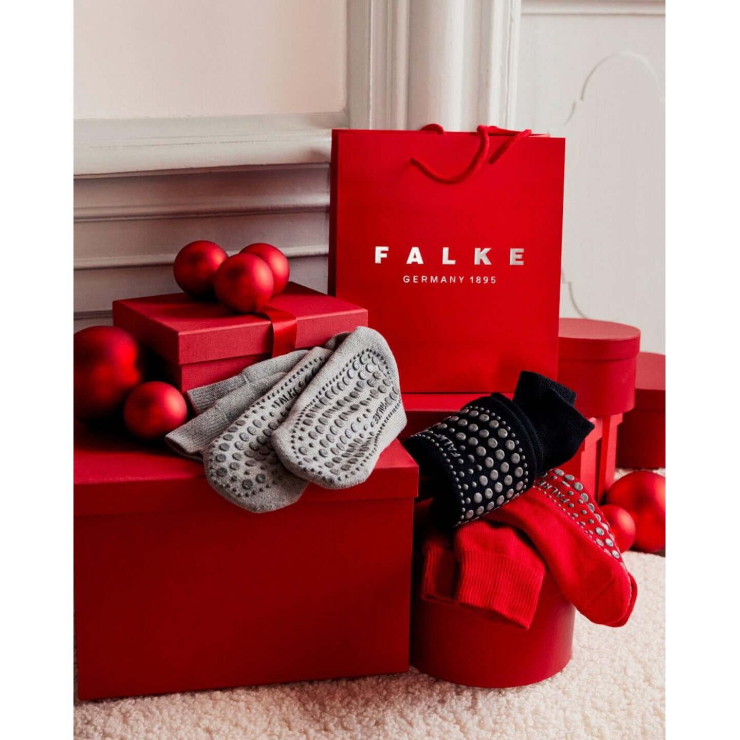 Chaussettes Homepads FALKE en textures grises, noires et rouges, présentées avec des boîtes rouges et boules décoratives.