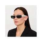 Lunettes de soleil Flick blanches avec verres noirs, offrant élégance et protection UV, portées par une femme.