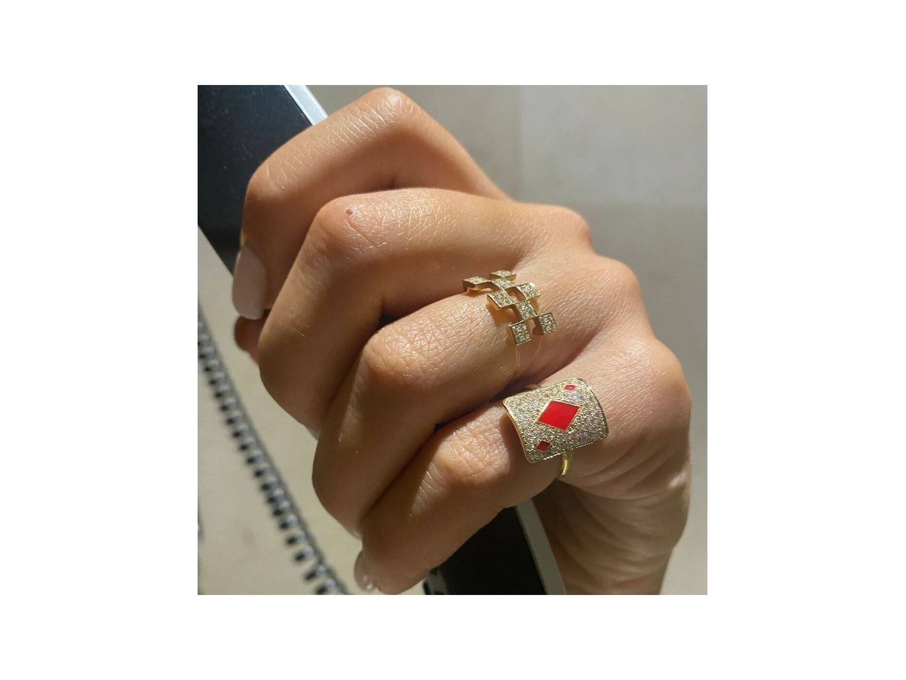 Close-up of a hand wearing two elegant rings, one gold with diamonds and the other with a red gemstone.