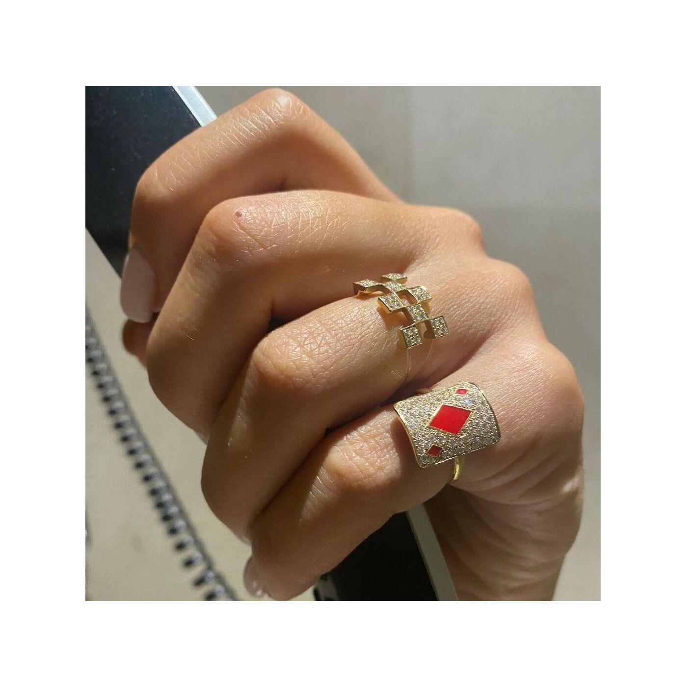 Close-up of a hand wearing two elegant rings, one gold with diamonds and the other with a red gemstone.