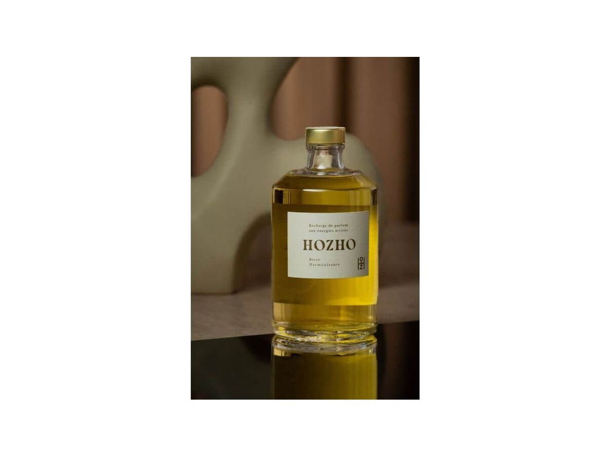 Bouteille d'huile Hozho sur une surface réfléchissante avec fond artistique, mettant en avant une présentation raffinée.