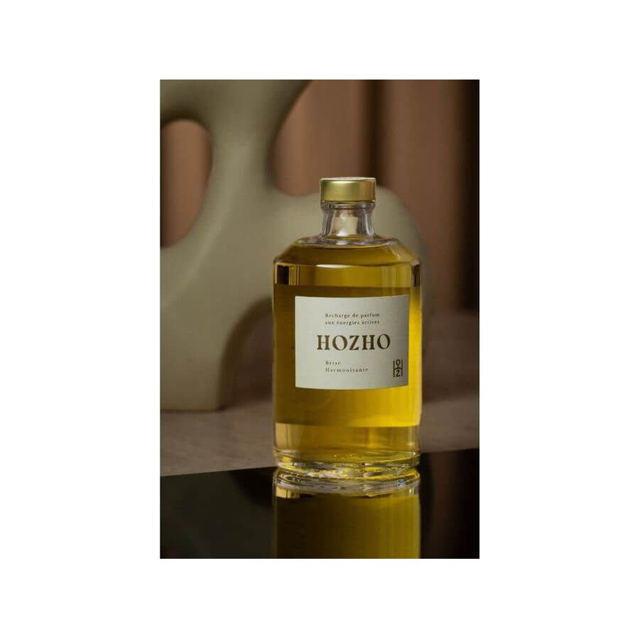 Bouteille d'huile Hozho sur une surface réfléchissante avec fond artistique, mettant en avant une présentation raffinée.