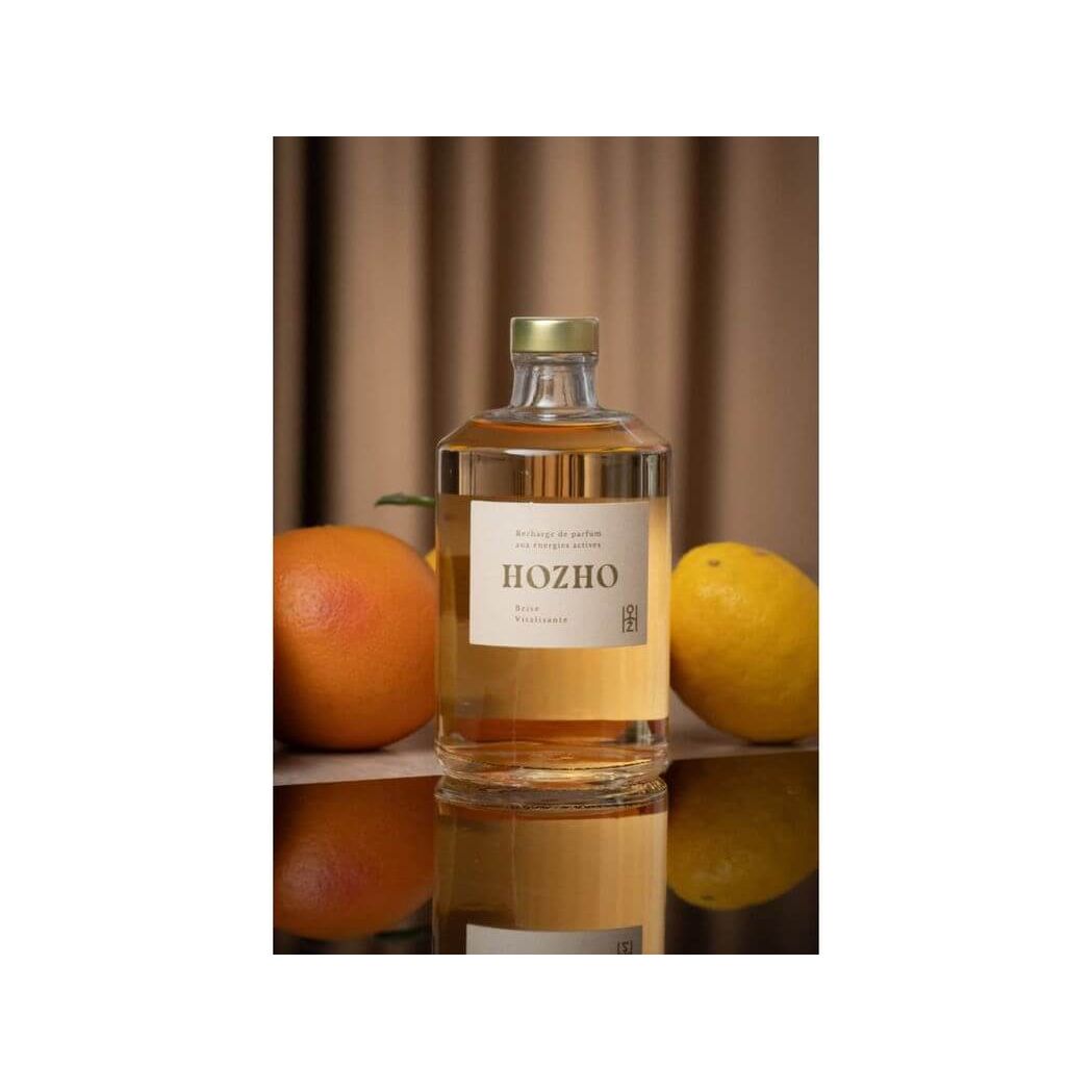 Bouteille de diffuseur HOZHO entourée d'orange et de citron, évoquant une atmosphère revitalisante.